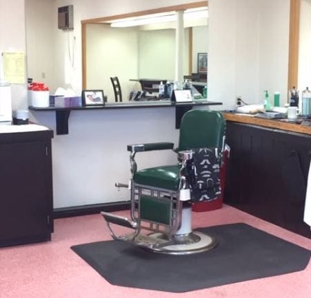 A green leather barber chair at Toby's, facing the mirror and the tool counter